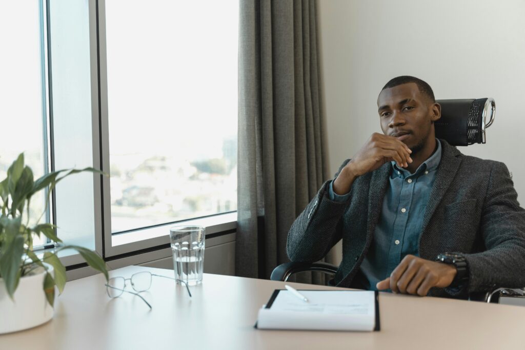 Professional man in a thoughtful pose at an office desk with city view.