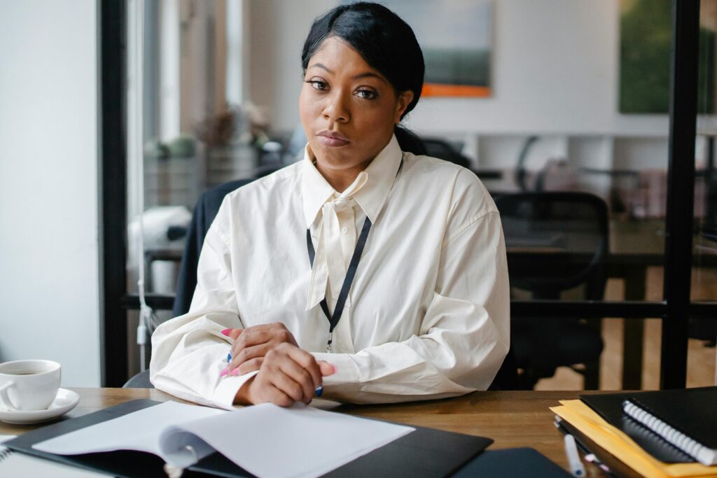 Calm African American businesswoman in formal outfit sitting at desk with papers in modern office and looking at camera